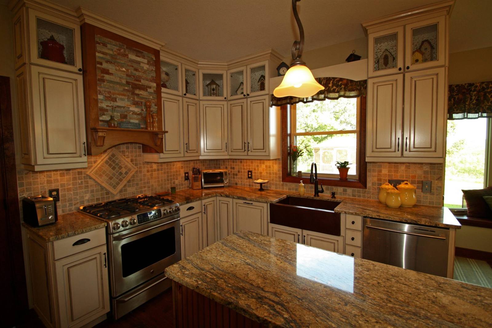 Zaxx kitchen with cream glazed cabinets, glass-front uppers, copper farmhouse sink and granite island